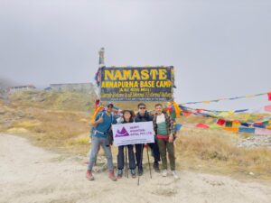 Happy Mountain Nepal team taking group picture with the sign of Annapurna Base Camp