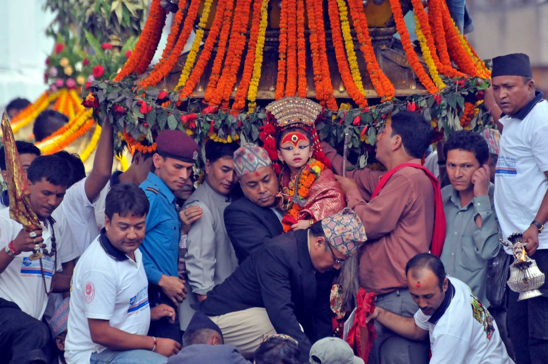A vibrant, slightly overhead shot captures a group of men, mostly in traditional or semi-traditional attire, resting or sleeping amidst rich floral decorations, likely during a cultural or religious ceremony in Nepal.