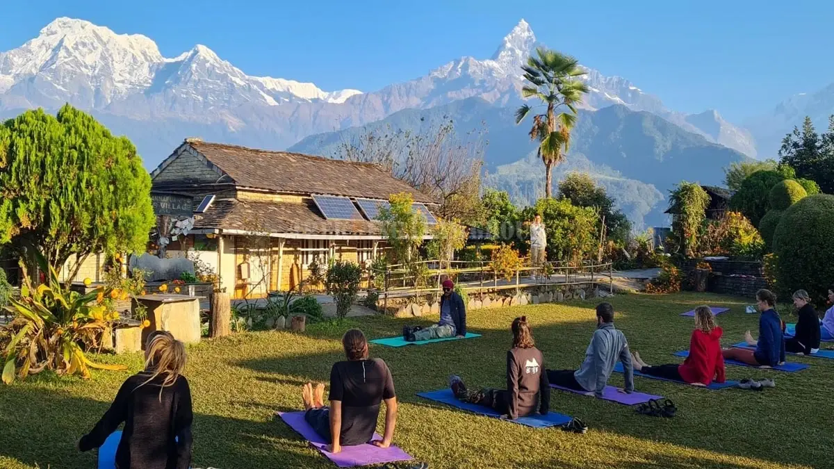 A group of people practicing yoga outdoors in Nepal, with mountains and a village in the background