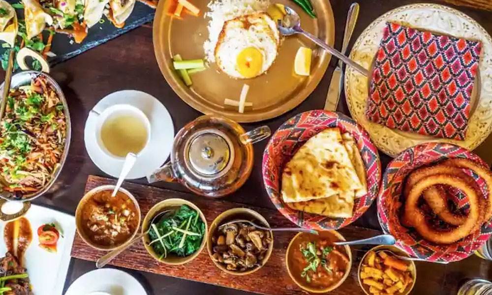 A flat lay shot of a traditional Nepali thali or platter, featuring various dishes. The central elements include a round metal plate with steamed rice, a fried egg, and what appears to be a lentil soup (dal) in a bowl.