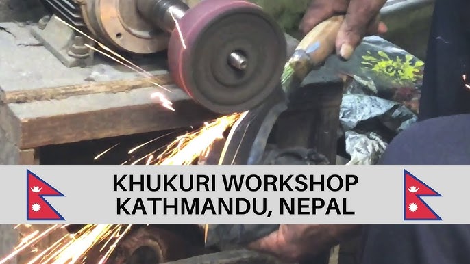 Close-up of a blacksmith sharpening a Khukuri knife on a grinding wheel, with sparks flying in a workshop in Kathmandu, Nepal. The image also displays text indicating 'KHUKURI WORKSHOP KATHMANDU, NEPAL