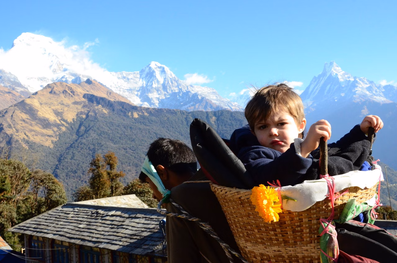 An image of a young child being carried in a traditional Nepali basket, known as a doko, on a mountain trail.