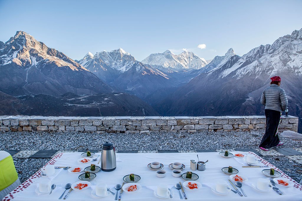 Breakfast table in the foreground and majestic, snow-capped kondge mountains in the background, is visually similar to locations found in the Himalayas, specifically around areas like the Annapurna Base Camp, Ladakh, and Uttarakhand.
